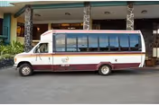 A white and maroon passenger shuttle bus parked under the entrance awning of a building with stone columns.