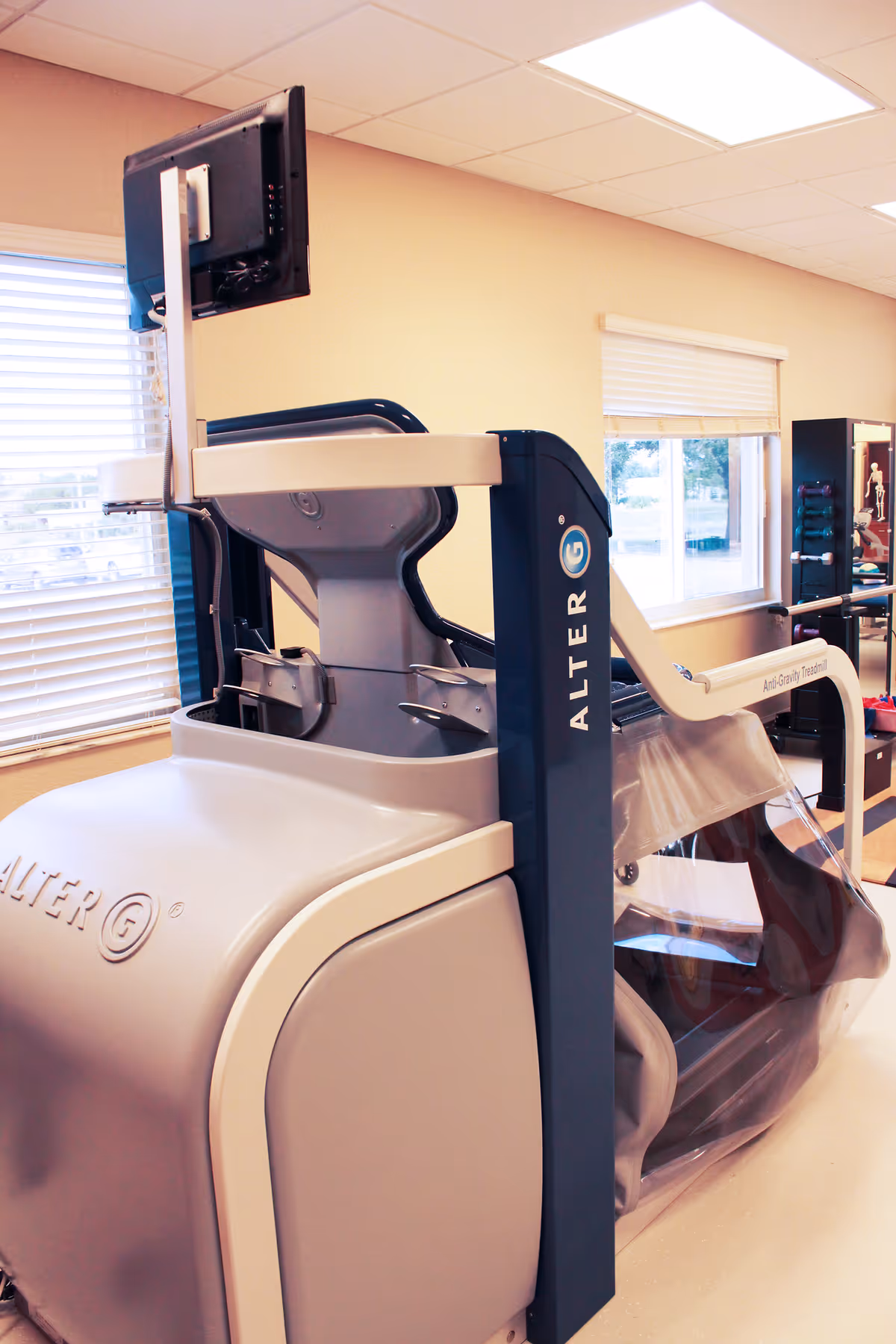 A piece of rehabilitation exercise equipment called AlterG Anti-Gravity Treadmill in a room with windows and blinds, designed to assist with physical therapy and walking exercises.