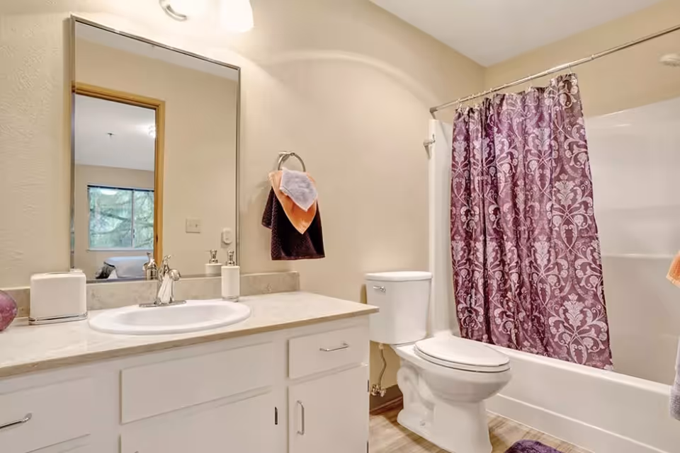 A clean bathroom featuring a vanity with sink and mirror, a toilet, and a bathtub with a purple patterned shower curtain.