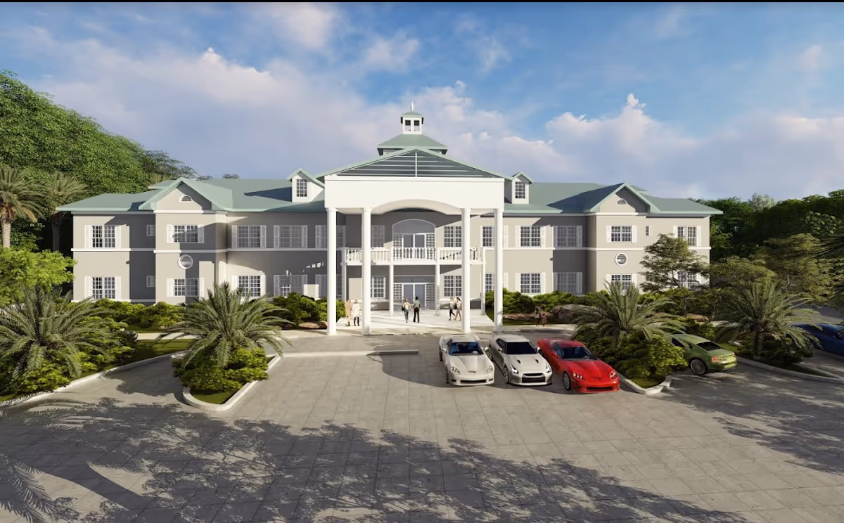 Front exterior view of a large, two-story senior living facility building with a green roof, white columns at the entrance, several windows, and landscaped greenery including palm trees. There are cars parked in front and a few people walking near the entrance under a partly cloudy sky.