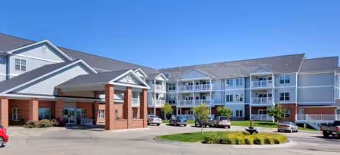 Exterior view of Kinship Pointe Northridge senior living building with parked cars and landscaped entrance.
