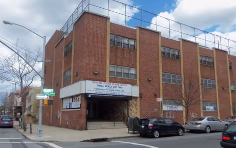 Brick exterior building with entrance and parked cars on a city street.