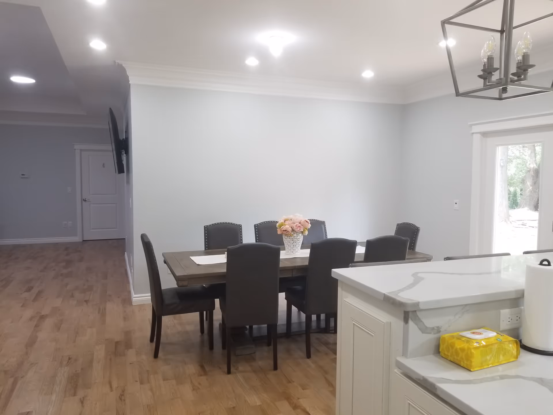 Open dining area with a wooden table, six upholstered chairs and a floral centerpiece next to a kitchen island.