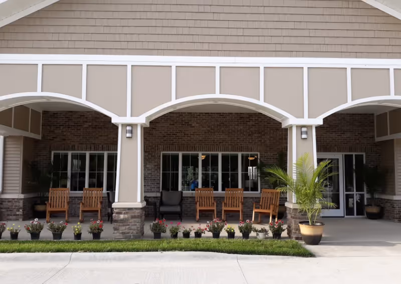 Covered front porch with arched columns, wooden chairs, potted plants, and large windows.