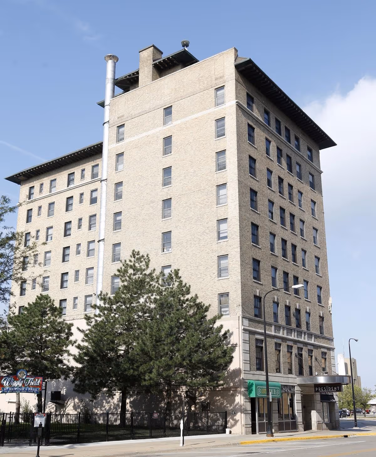 Exterior view of a multi-story brick building named Hotel President Apartments with several windows, trees in front, and a sidewalk along the street.