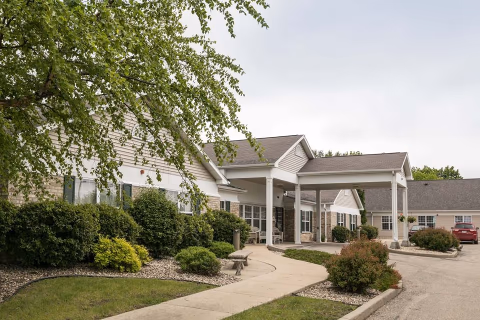 Covered entrance and driveway of Madison Pointe Senior Living with a walkway and landscaped shrubs in front of the building.