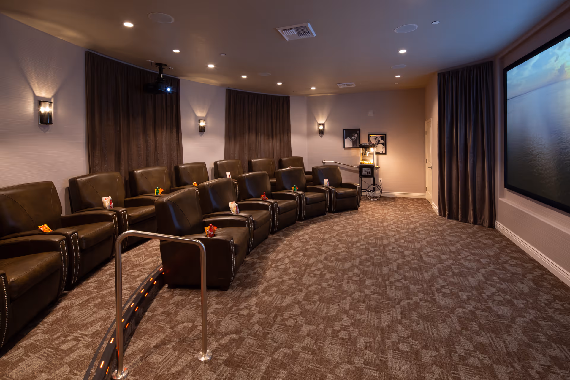 Interior movie/theater room with rows of leather recliners facing a large screen and a popcorn machine.