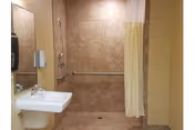 Accessible bathroom with a wall-mounted sink, mirror, grab bars and a walk-in tiled shower with a yellow curtain.