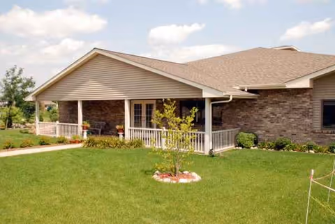 Single-story care facility exterior with a covered front porch, white railing, and well-kept lawn.