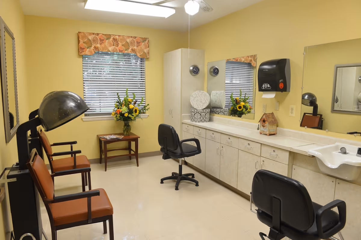 Small salon room with styling chairs and hooded hair dryers, mirrors, a sink and a vase of flowers on the counter.