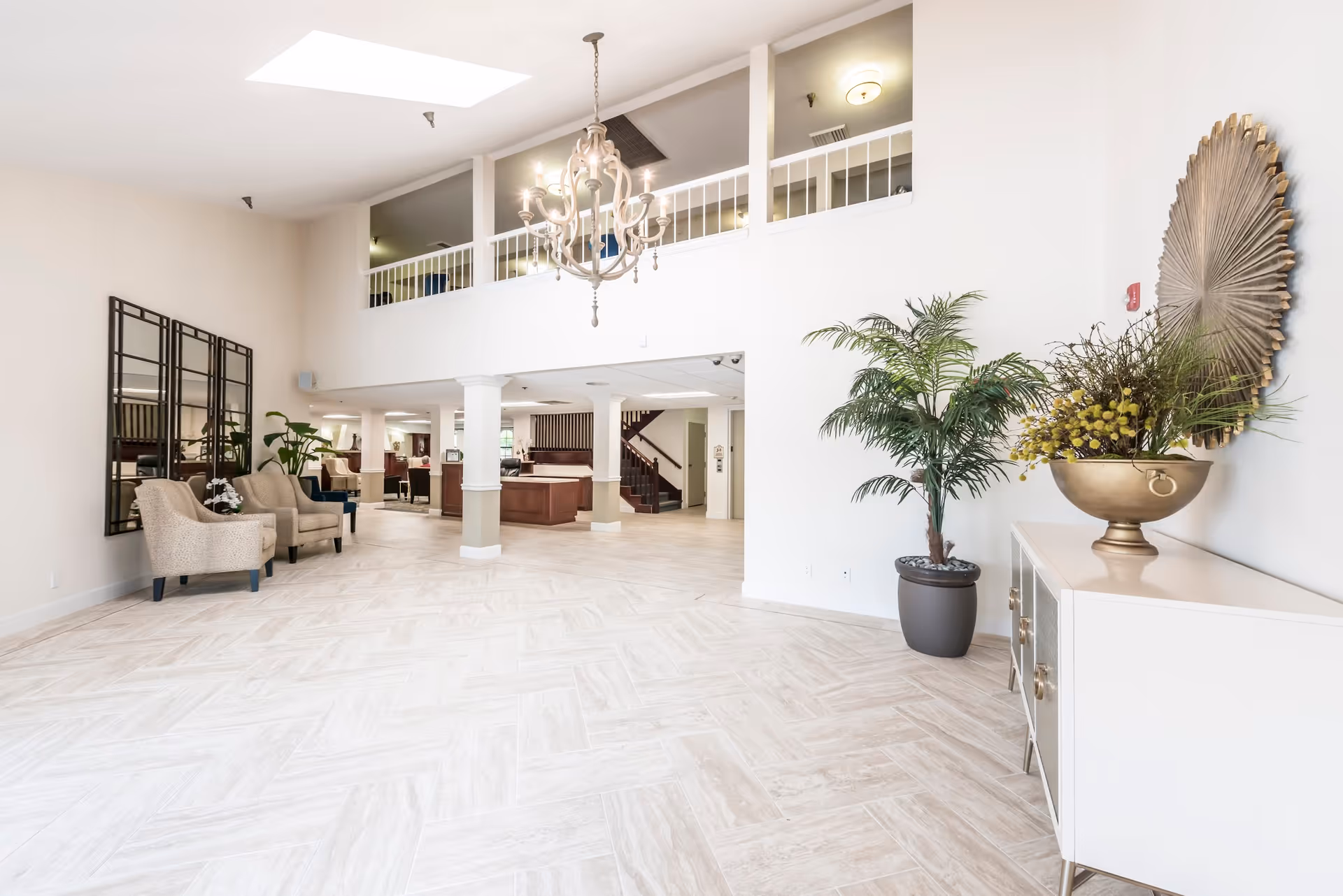 Bright, open two-story lobby with seating, a chandelier, potted plants, and a decorative console.