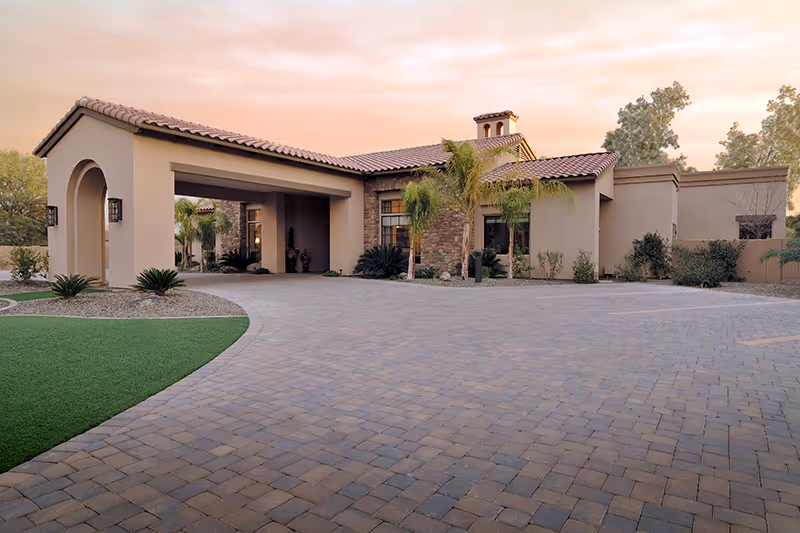 Single-story southwestern-style building with a tiled roof, porte-cochere, paved driveway and desert landscaping at sunset.