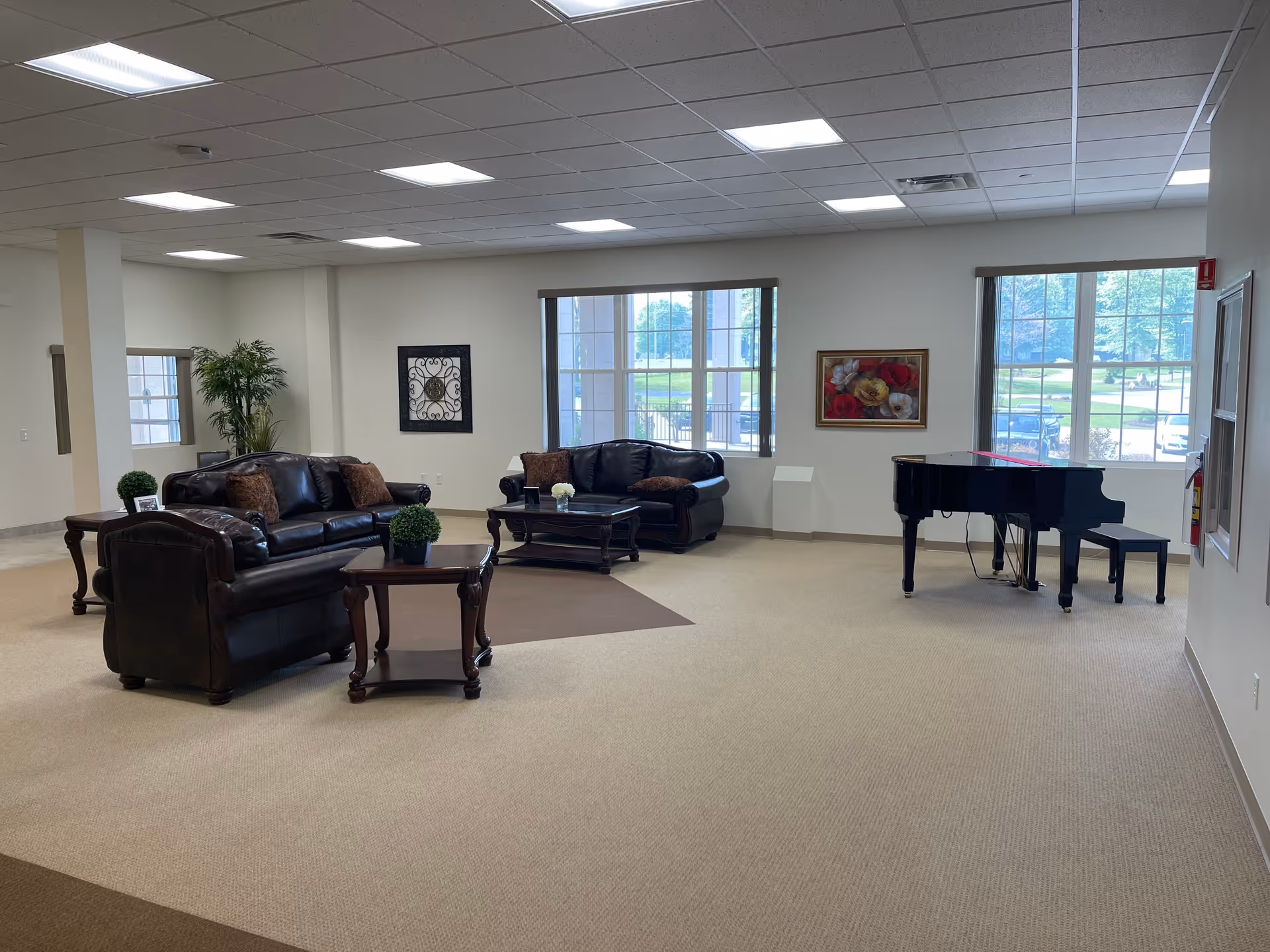 Spacious senior living common room with leather sofas, coffee tables, large windows, and a grand piano.