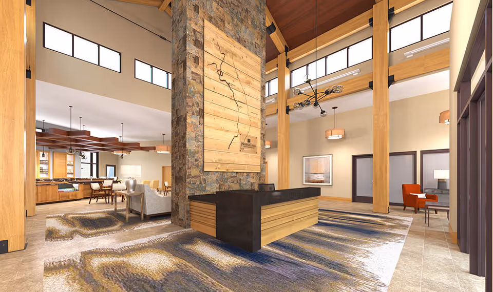 Spacious and well-lit interior of a senior living facility featuring a large stone and wood reception desk in the center, high ceilings with wooden beams, modern light fixtures, and a patterned carpet. The background shows a dining area with tables and chairs, and a cozy seating area with armchairs and a sofa.