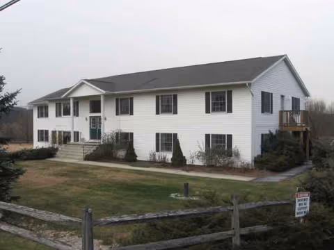 Exterior of a white, two-story senior living home with a front yard and fence.