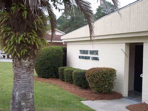 Exterior view of Tebeau House facility with entrance and trimmed hedges.
