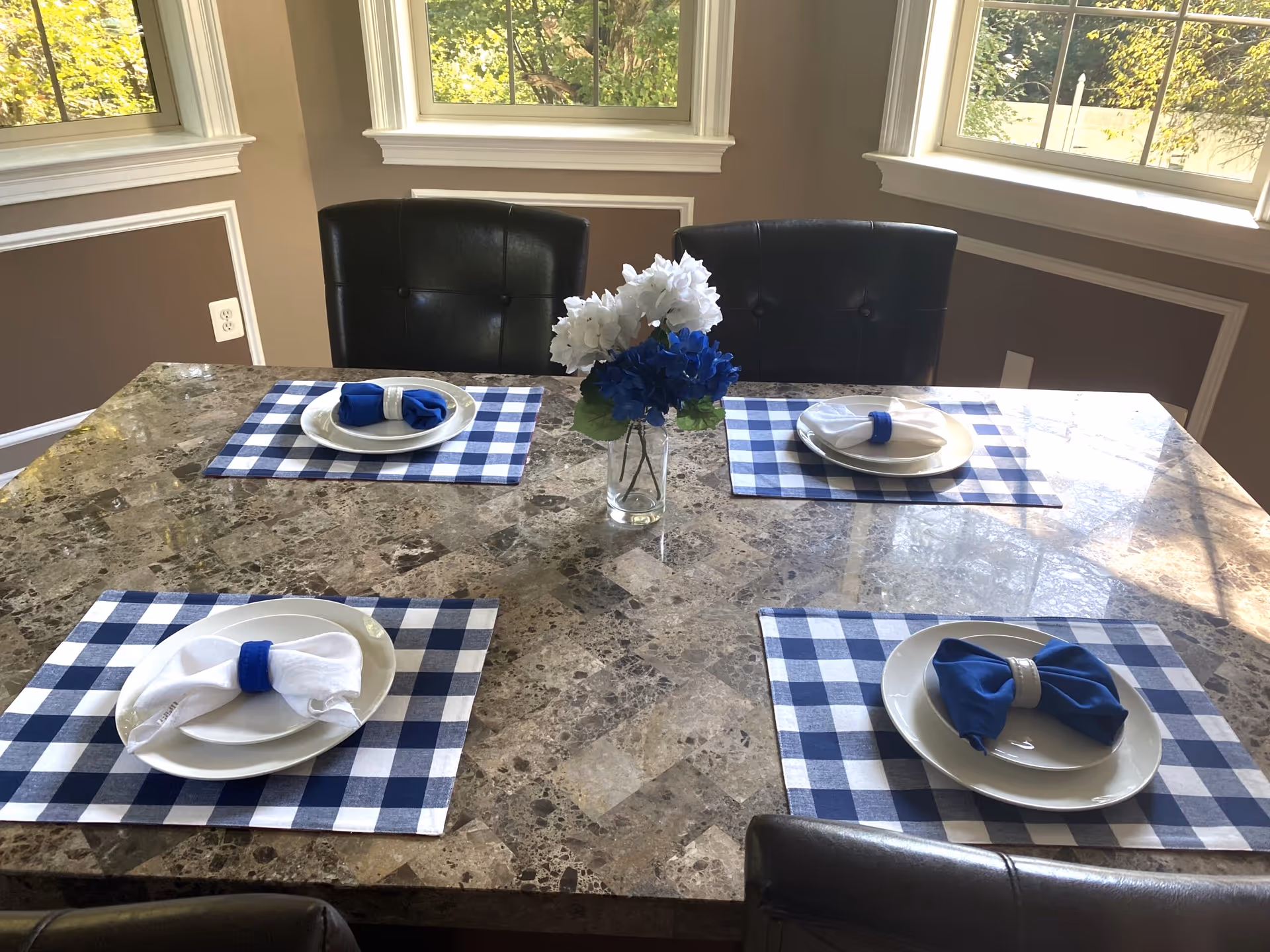 A granite dining table set with blue-check placemats and napkins in a bright room.