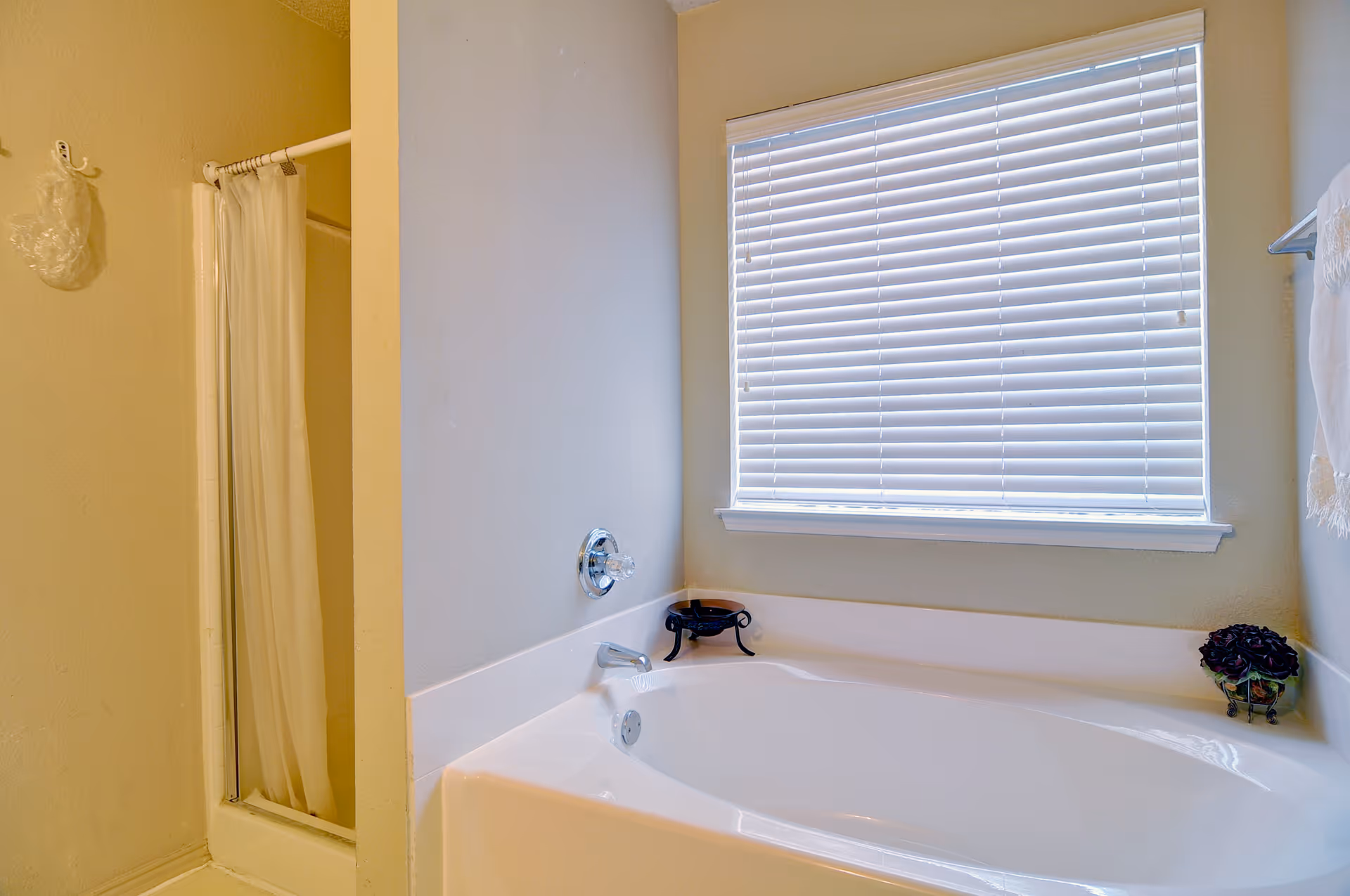Bright bathroom featuring a bathtub, a separate shower with a curtain, and a window with closed blinds.