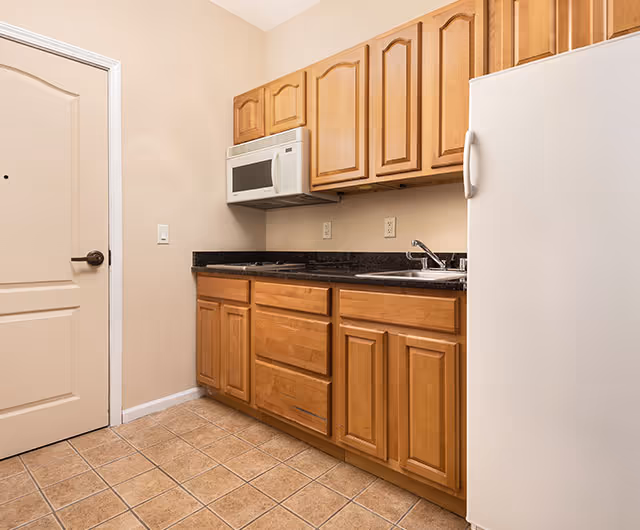 Small kitchen with wooden cabinets, black countertop, white microwave, sink, and refrigerator.