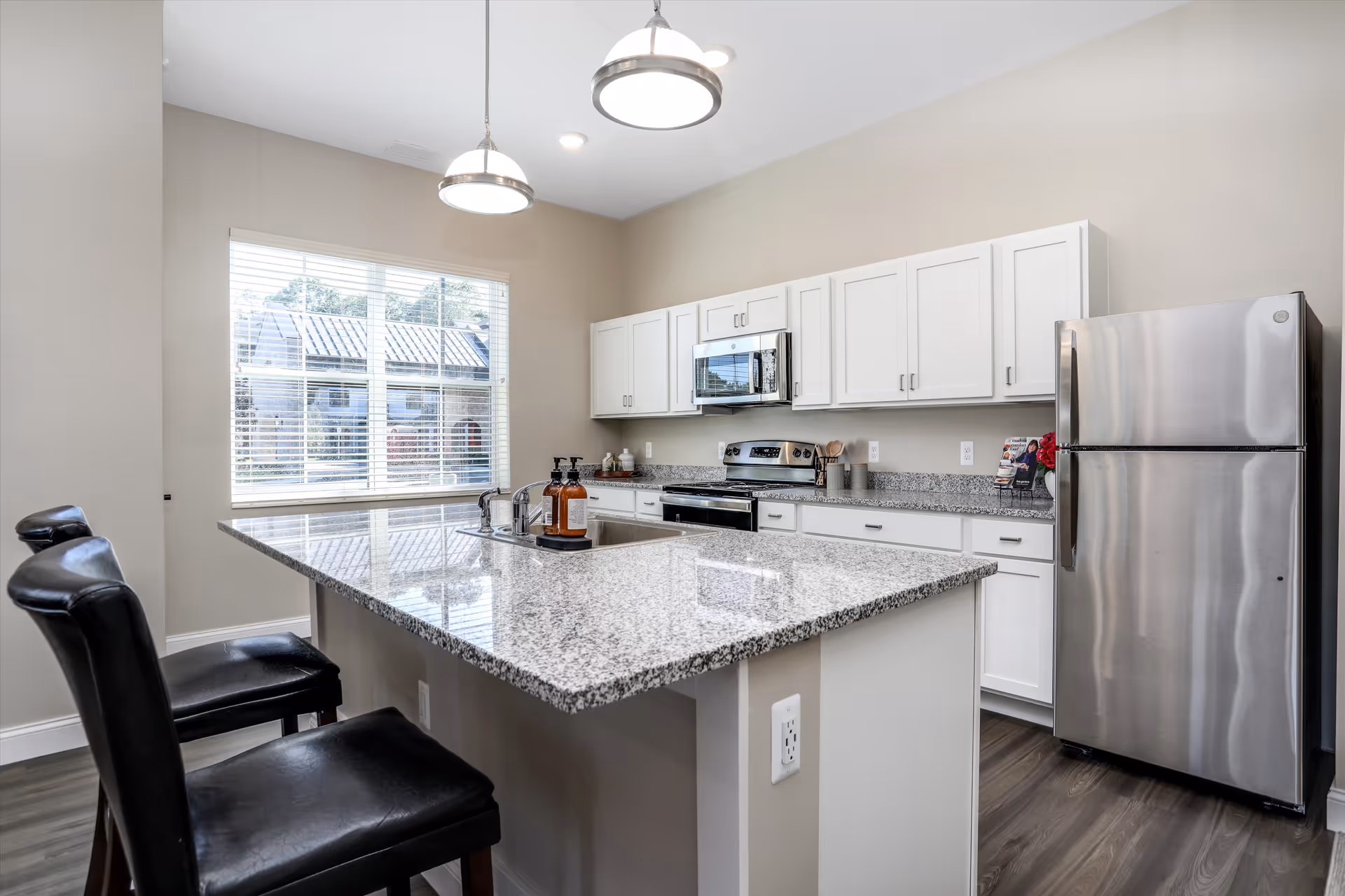 Bright modern kitchen with a large granite island, stainless steel appliances, white cabinets, and bar stools.