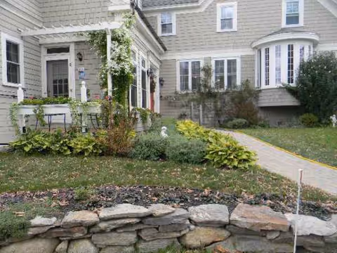 Front exterior of a senior living house with a garden and stone wall.