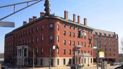 A large red brick multi-story building on a street corner with arched windows.