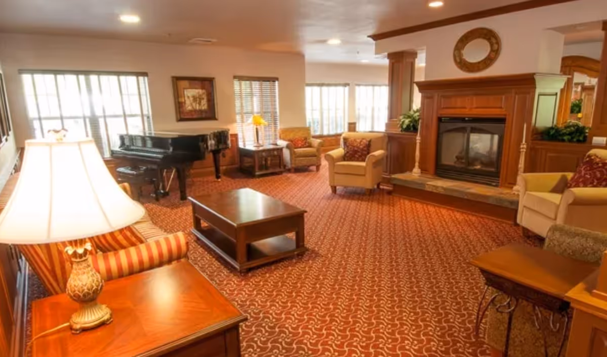 Spacious furnished lounge with armchairs, coffee table, fireplace, and a grand piano.