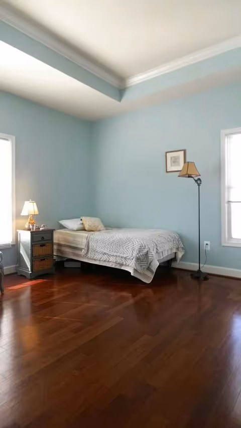 A softly lit bedroom with a single bed, nightstand, and floor lamp.