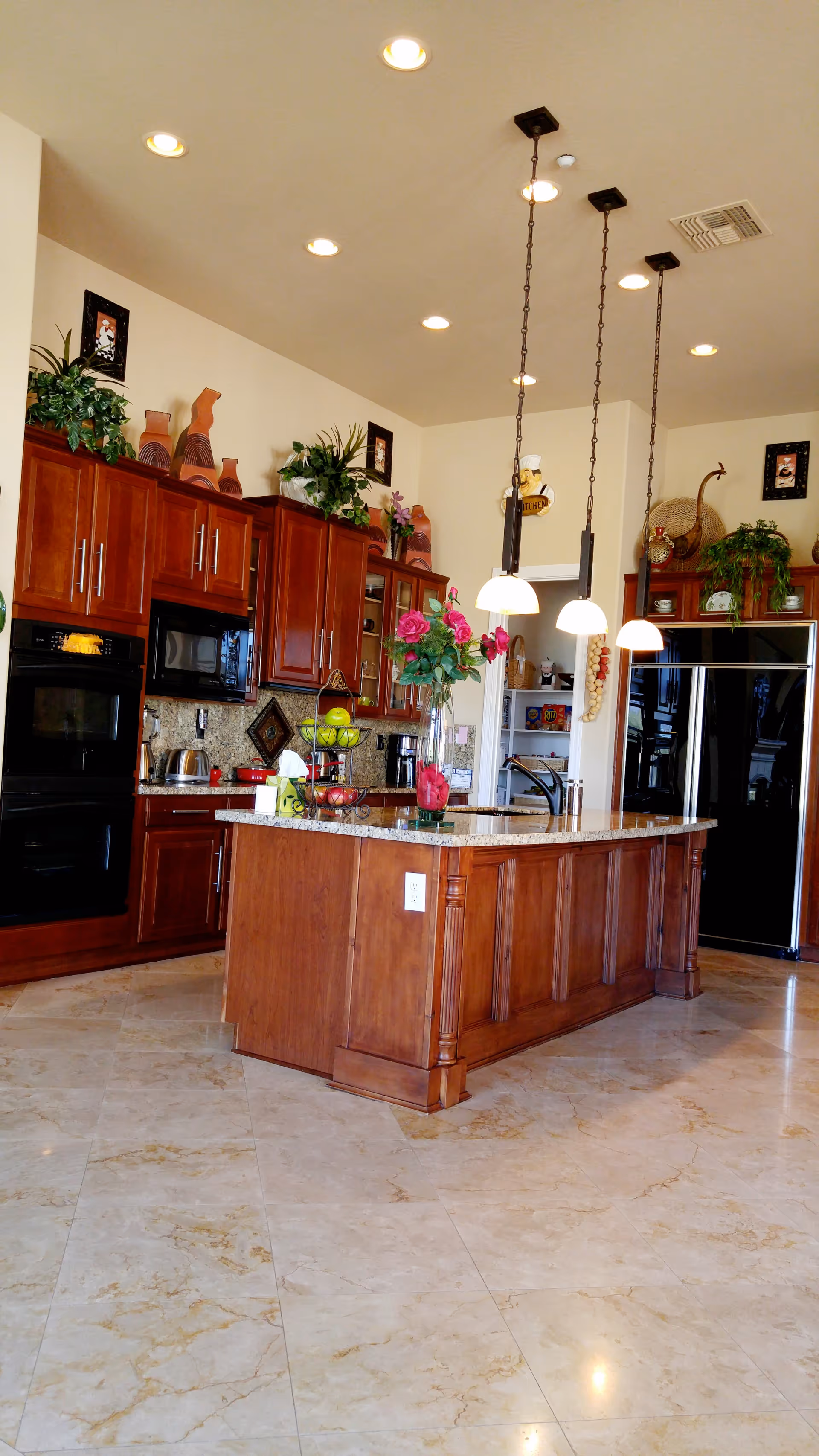 Spacious kitchen with a central wooden island, hanging pendant lights, cherry cabinets, stainless appliances and marble tile floor.