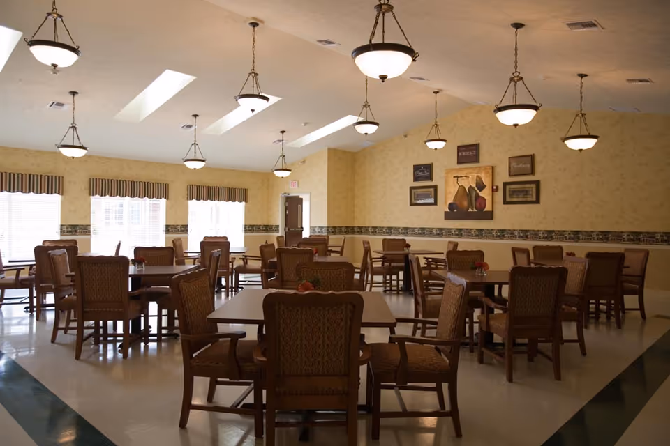 Well-lit dining room with multiple wooden tables and upholstered chairs under pendant lights and skylights.
