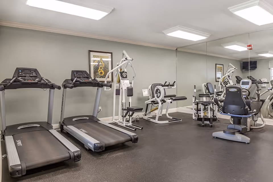 Fitness room with treadmills, weight machines, and exercise bikes in front of a mirrored wall.
