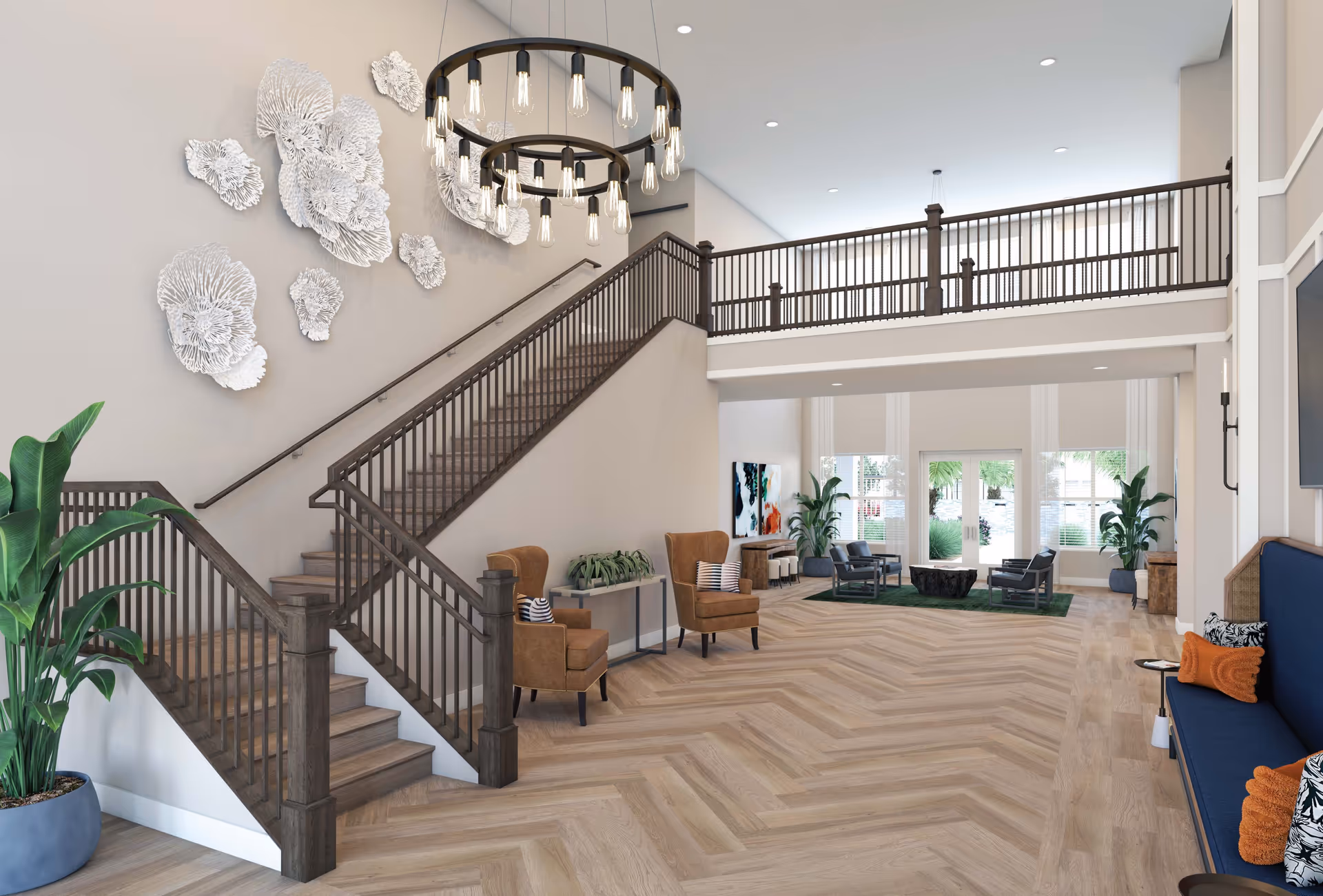 A spacious and modern interior common area with a wooden staircase featuring dark railings, two brown armchairs with striped pillows, a large circular chandelier with exposed bulbs, decorative white wall art, potted plants, and a seating area with black chairs and a green rug near large windows and glass doors.