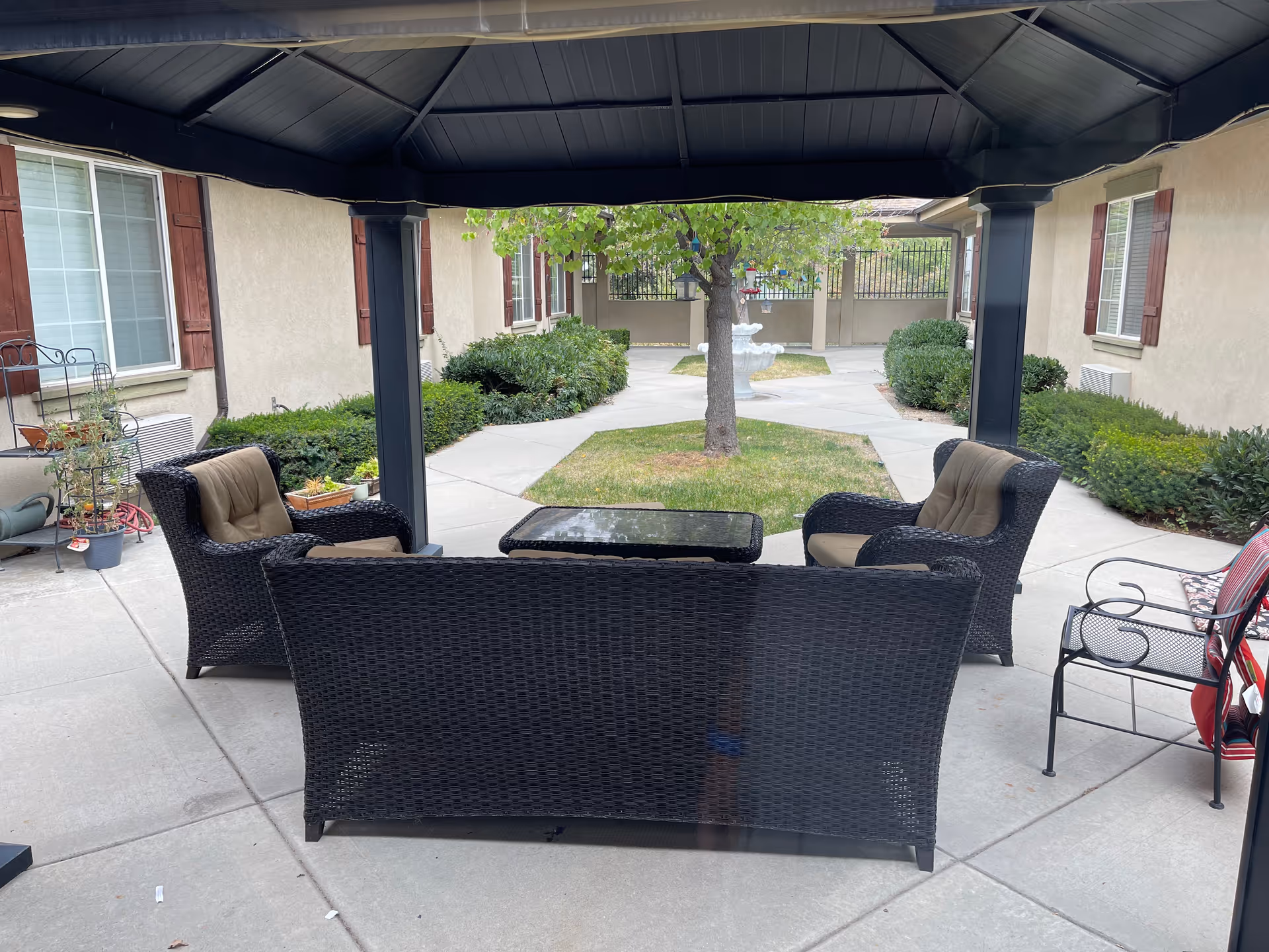 Outdoor covered seating area with wicker sofa and chairs overlooking a courtyard with a tree and fountain.