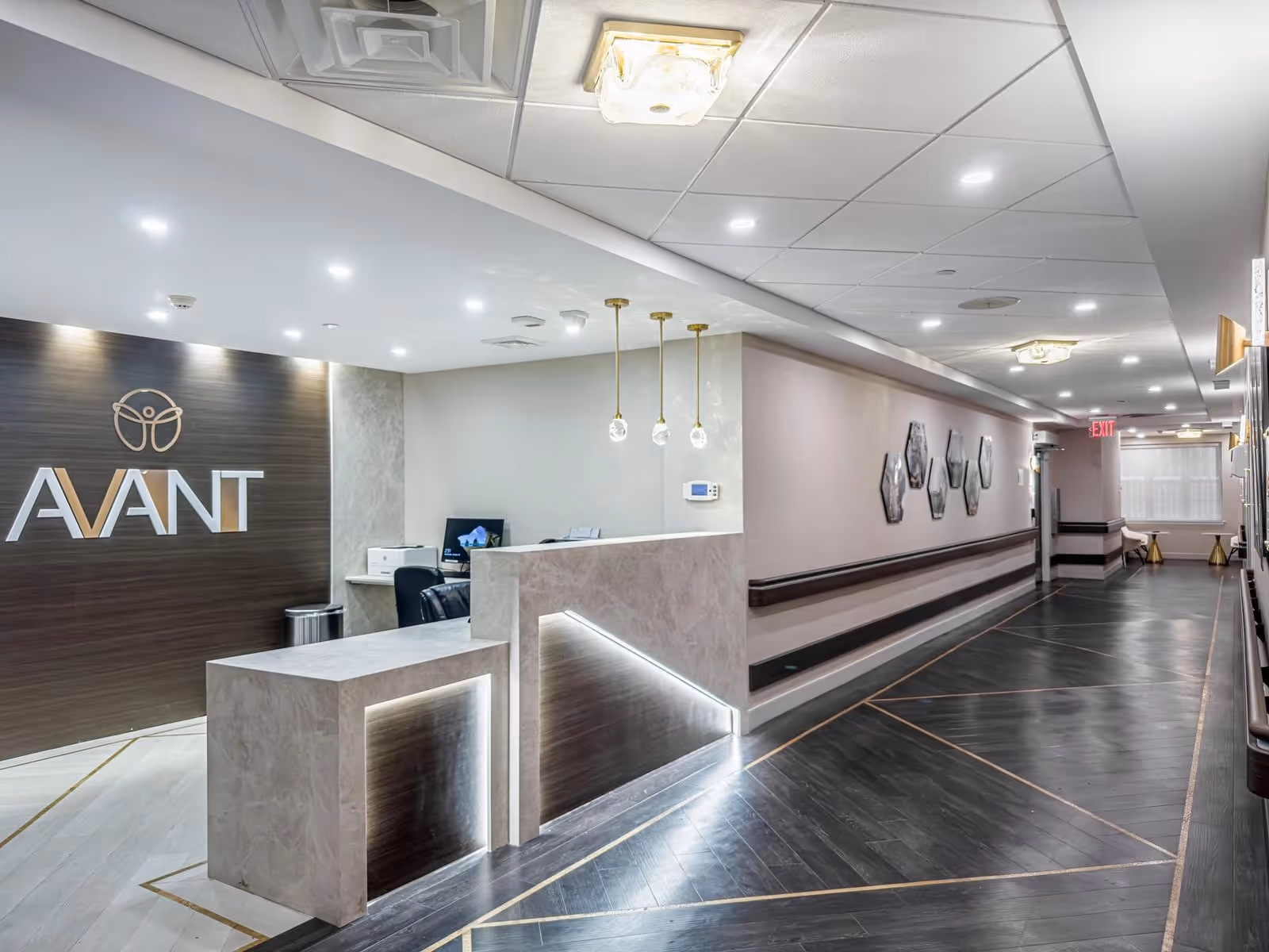 Reception area with a marble front desk, a dark wood wall displaying the AVANT logo, and a long, well-lit hallway.