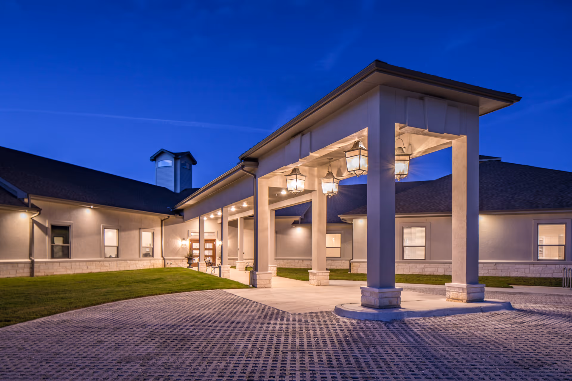 Dusk view of a single-story building entrance with a covered porte-cochere and hanging lanterns.