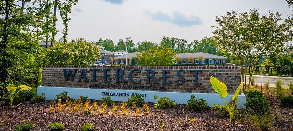 Brick entrance sign that reads "WATERCREST" with landscaping in front and the facility buildings visible behind.