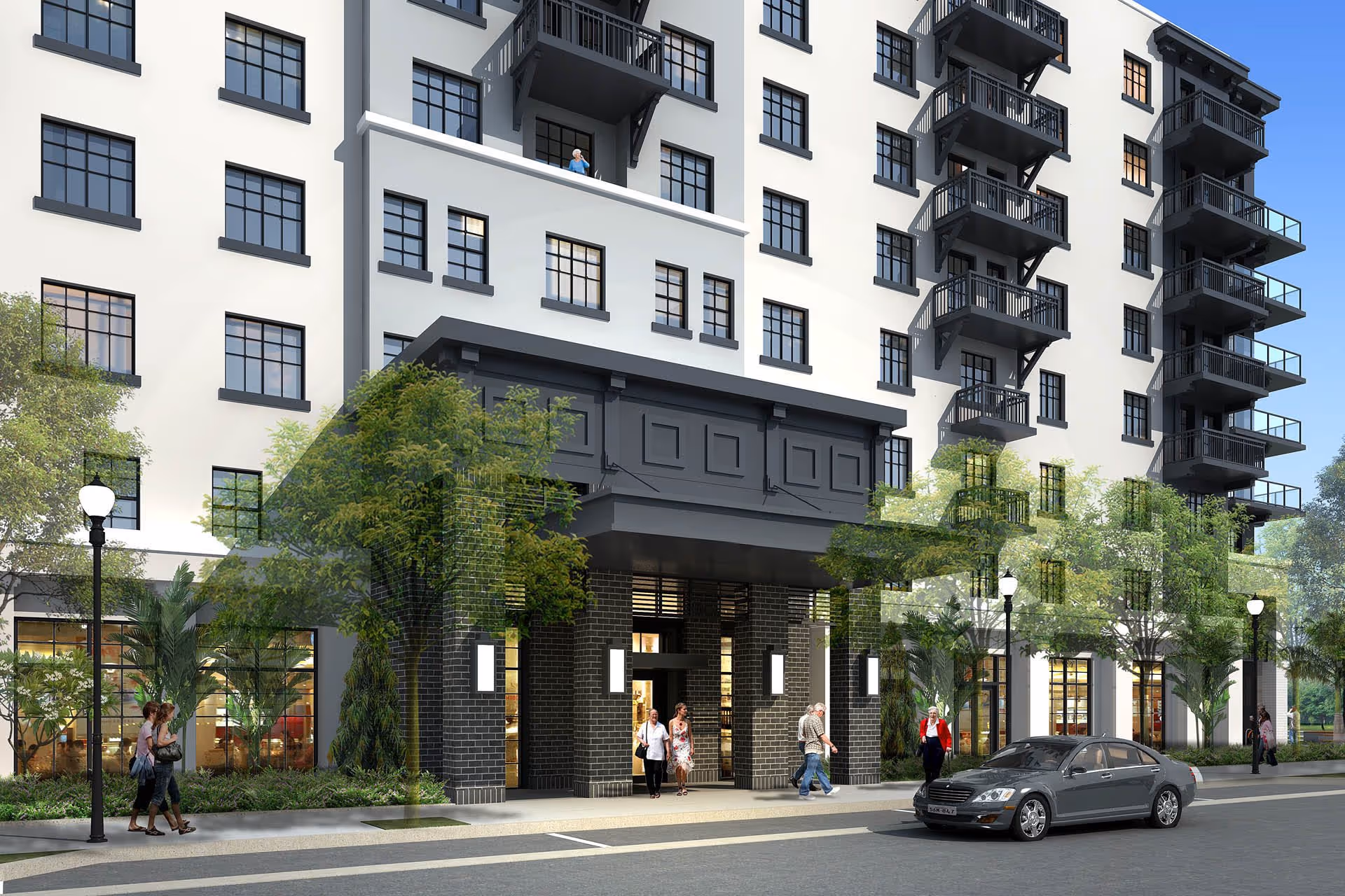 Exterior view of a multi-story residential building with black-framed windows and balconies. People are walking near the entrance, and a car is parked on the street in front. Trees and street lamps line the sidewalk.