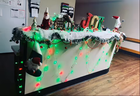 Reception desk decorated with Christmas lights, garlands, Santa figurines and large 'JOY' letters.