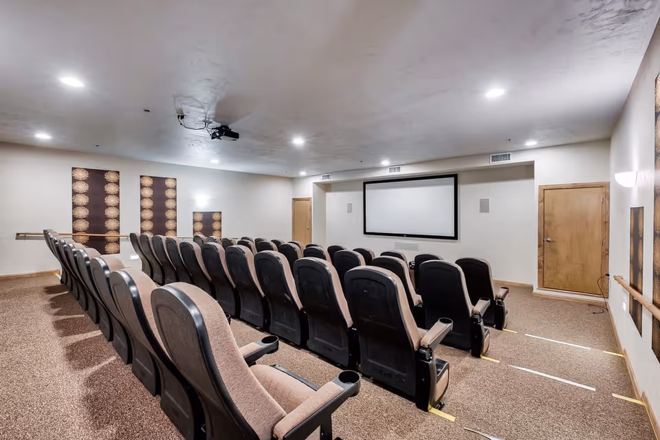 Small theater-style screening room with rows of upholstered seats facing a projection screen.
