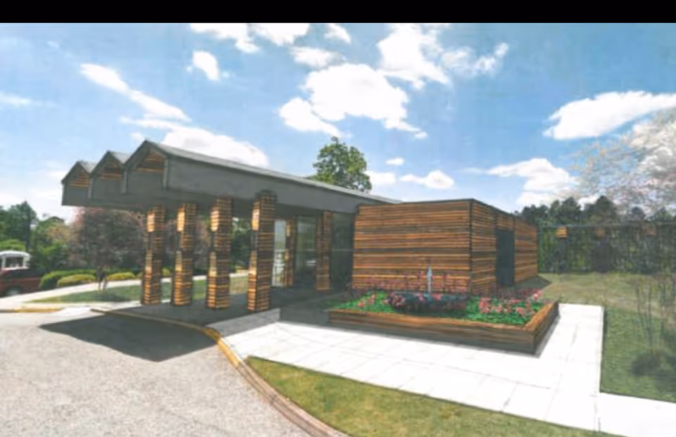 Modern single-story building entrance with a wooden-clad portico and landscaped planter under a blue sky.