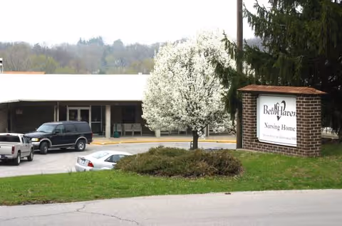 Exterior view of a senior living facility with a brick sign and blooming tree.