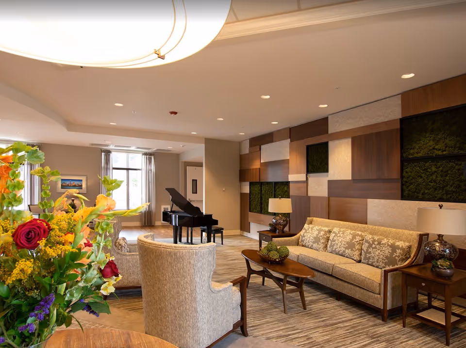 Well-appointed common room with sofas, armchairs, a coffee table, a grand piano and a large floral arrangement.