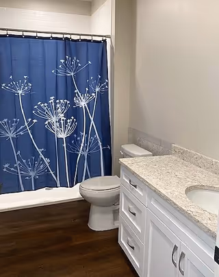 Bathroom with a white vanity and marble countertop, toilet, and a bathtub with a blue floral shower curtain.