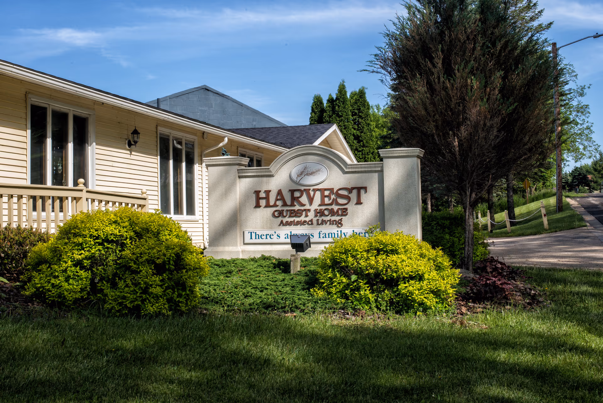 Front view of Harvest Guest Home sign and entrance with landscaped shrubs