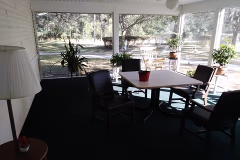 Screened sunroom with a square table and chairs, potted plants, and a view of the lawn outside.
