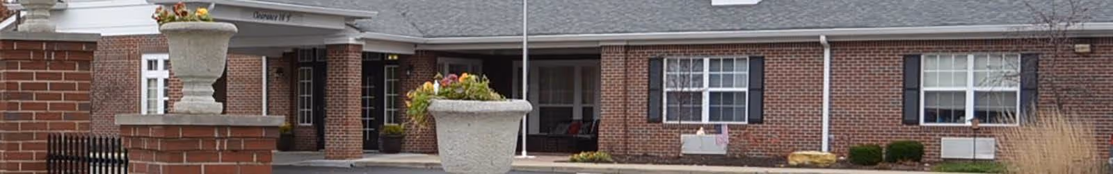 Front exterior of a single-story brick senior living building with a covered entrance, large planters, and windows.