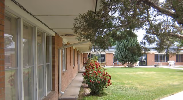 Exterior courtyard of a single-story brick care center showing a covered walkway, windows, shrubs, and a grassy lawn.
