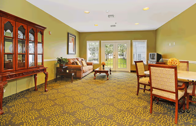 Bright common room with a sofa, coffee table, dining table and chairs facing glass doors that open to a lawn.