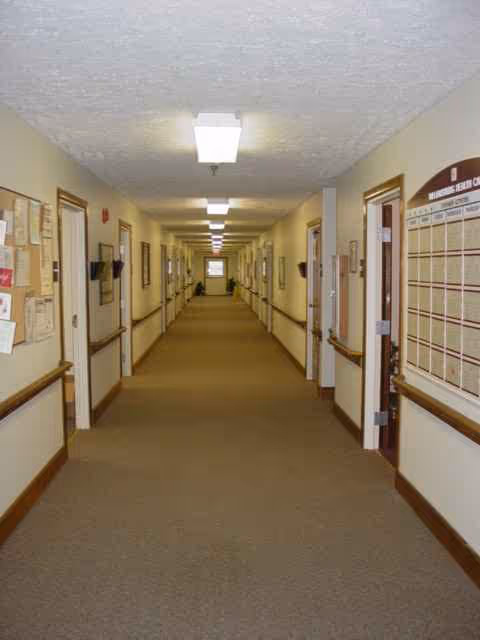 Long, well-lit hallway in a senior living facility with bulletin boards along walls.