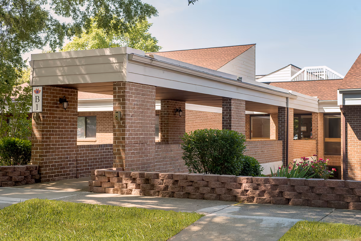 Covered brick entrance and walkway of a single-story building with landscaping and a 'B1' sign.